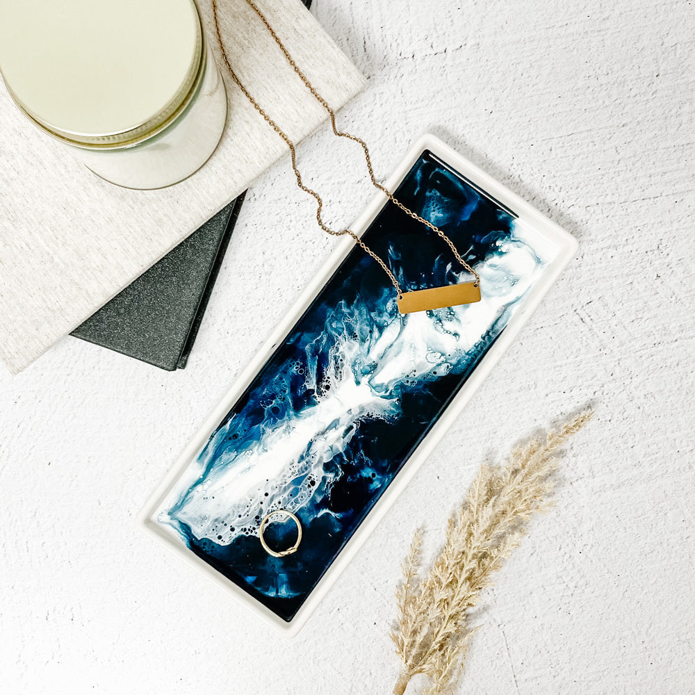 Jewelry set with necklace and ring on a ceramic resin tray next to a candle and notebook on a light surface. Available at Be Charmed