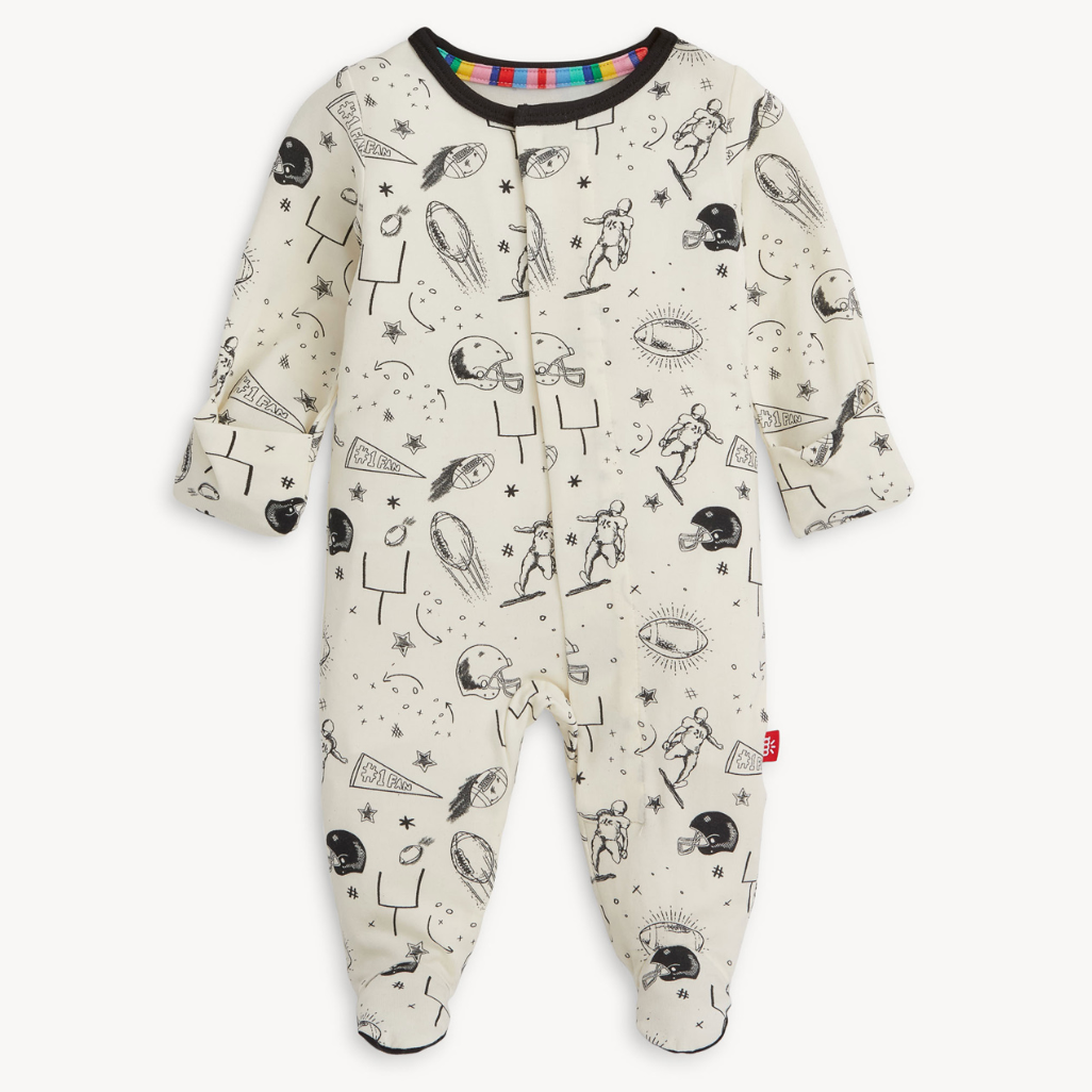 Magnetic Me baby footie in Natural Game Day print with sports icons. Soft modal fabric with magnetic closures for easy dressing. Available at Be Charmed.