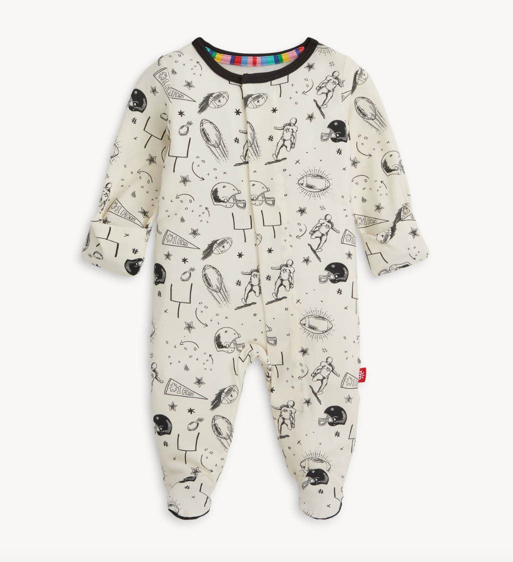 Magnetic Me baby footie in Natural Game Day print with sports icons. Soft modal fabric with magnetic closures for easy dressing. Available at Be Charmed.