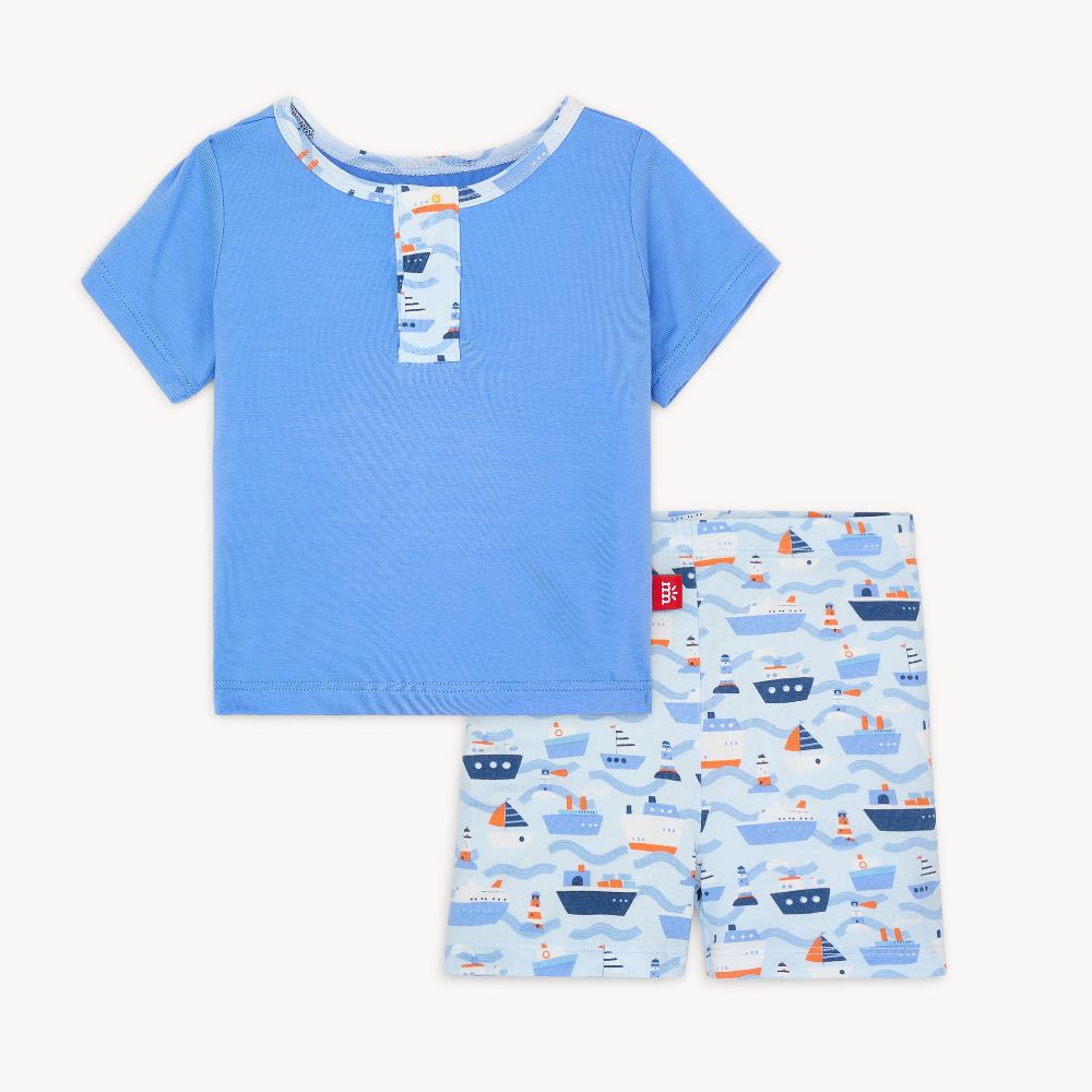 A set of children's clothing, with a blue short-sleeved top and shorts with a wave and surfboard print, featuring magnetic closures. Available at Be Charmed