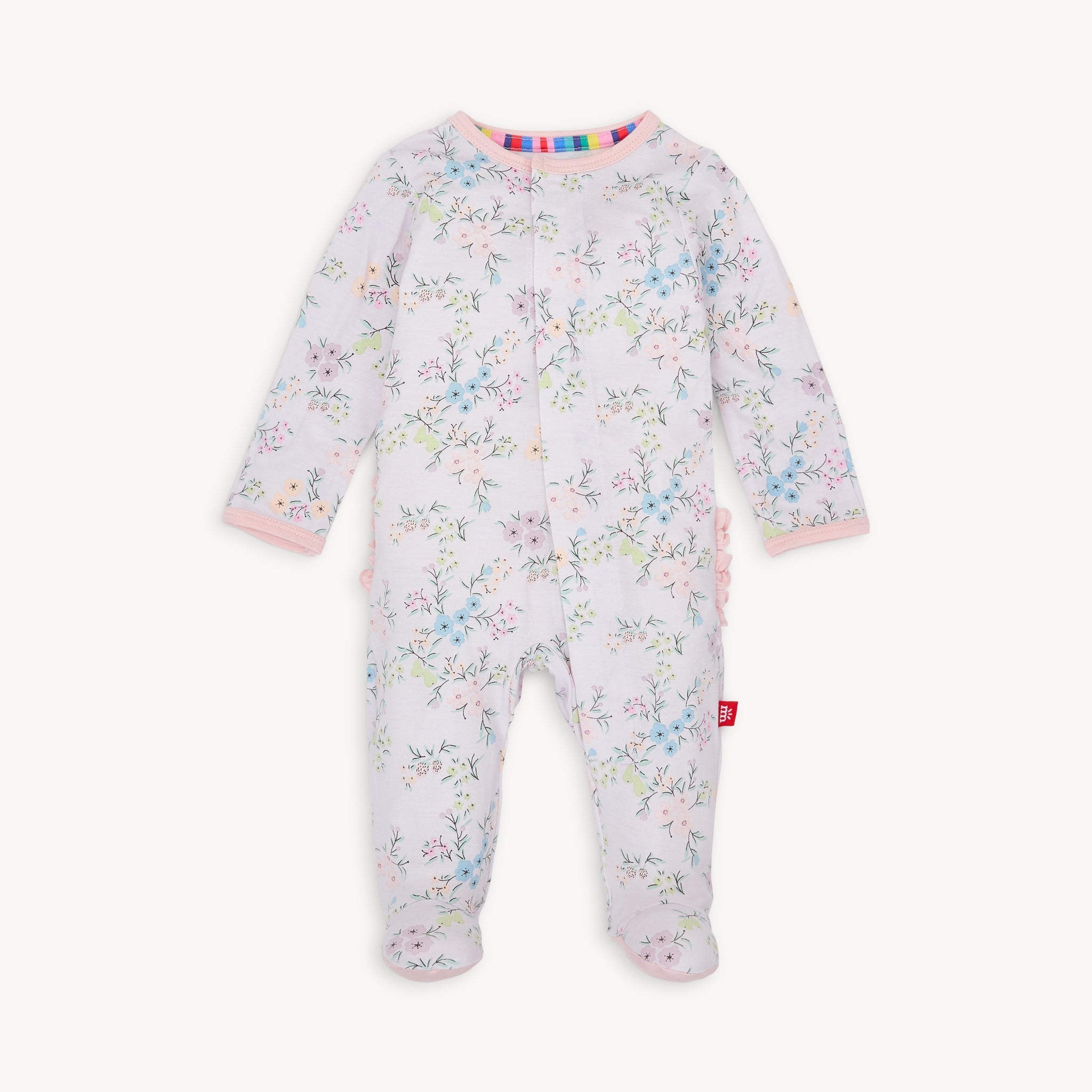 This image features the "Magnetic Me - Modal Footie with Ruffle - Emily," a charming and practical baby footie. It showcases a delicate floral pattern in soft hues, complemented by a ruffled trim at the feet. Available at Be Charmed