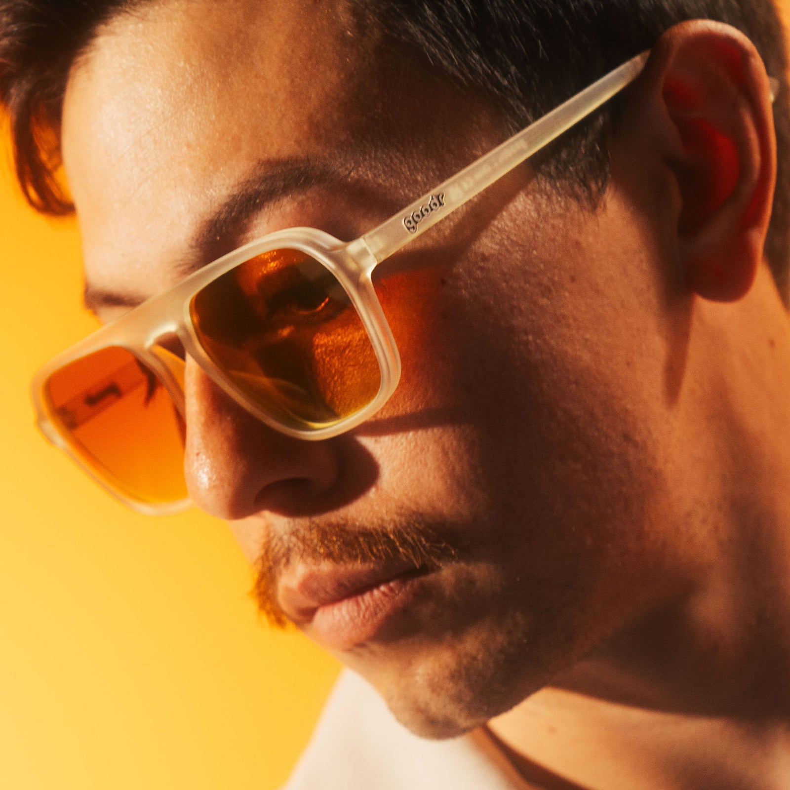 Close-up of a person wearing square sunglasses with a yellow-orange gradient on a bright yellow background. Available at Be Charmed