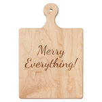 Wooden cutting board with 'Merry Everything!' engraving on a white background. Available at Be Charmed. 