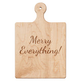 Wooden cutting board with 'Merry Everything!' engraving on a white background. Available at Be Charmed. 