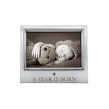 A silver-colored aluminum picture frame with a photo of a baby and a teddy bear, and the text 'A Star Is Born' on the bottom right. Available at Be Charmed