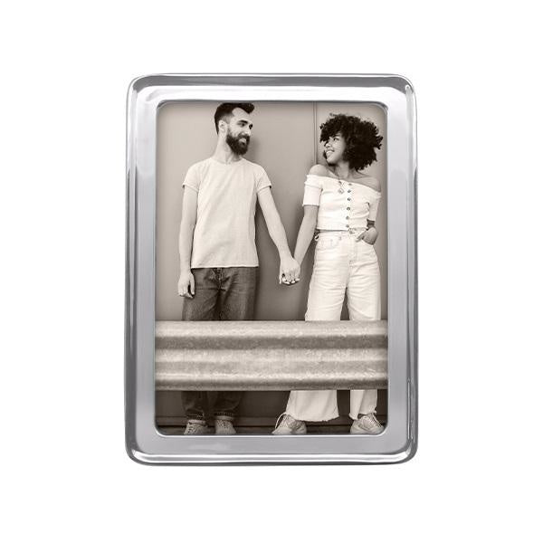A recycled aluminum 5x7 Mariposa picture frame with a transparent front, displaying an image of two people standing close by a wall. Available at Be Charmed