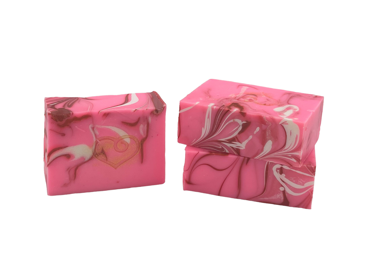 Two bars of Molly's Apothecary Lovespell bar soap, one stacked on top of the other. The top bar is pink with darker pink swirls, while the bottom one is white with darker white swirls. Available at Be Charmed