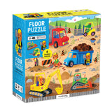 Box of a construction-themed floor puzzle for children, featuring colorful illustrations of vehicles and workers. Available at Be Charmed