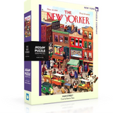 A puzzle box cover featuring a colorful illustration of a bustling Main Street scene with pedestrians and storefronts, titled 'The New Yorker'. Available at Be Charmed