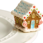 A mini gingerbread house charm placed on a white plate, with a festive design including a roof, windows, and door. Available at Be Charmed