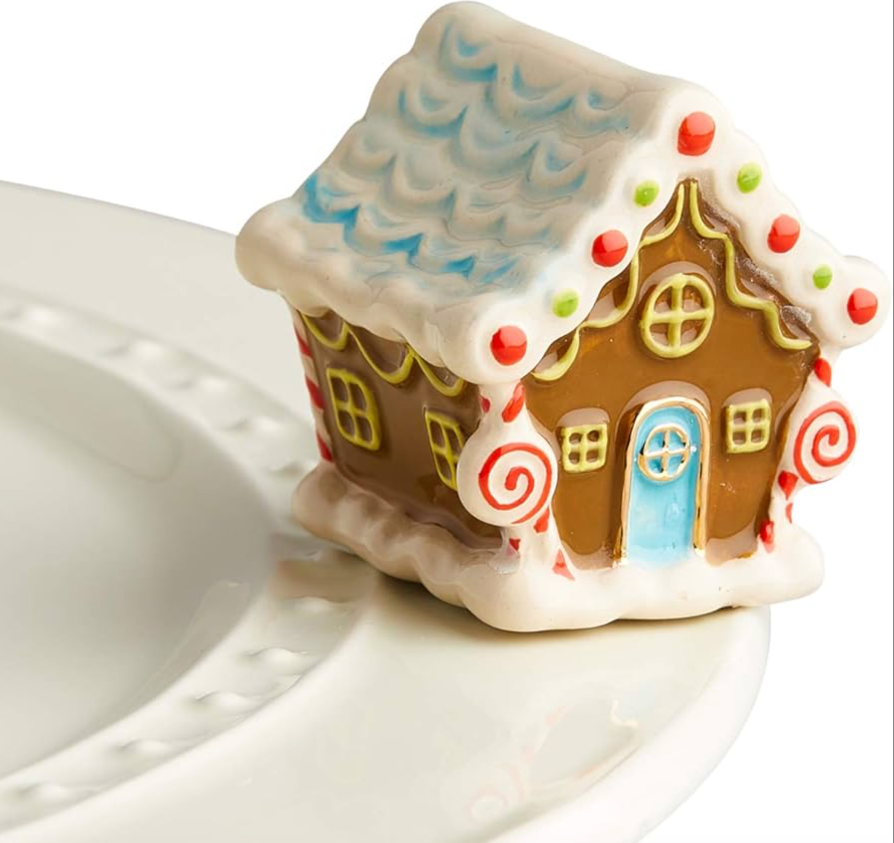A mini gingerbread house charm placed on a white plate, with a festive design including a roof, windows, and door. Available at Be Charmed