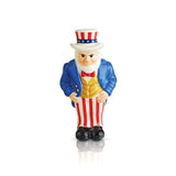 A ceramic figurine of Uncle Sam in a blue coat and hat with a red bow tie, standing on a round base which is not visible in the image. Available at Be Charmed