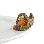 A small, decorative cornucopia-shaped dish charm, featuring autumn-colored fruits such as pumpkin and cranberry, placed on a white plate. Available at Be Charmed