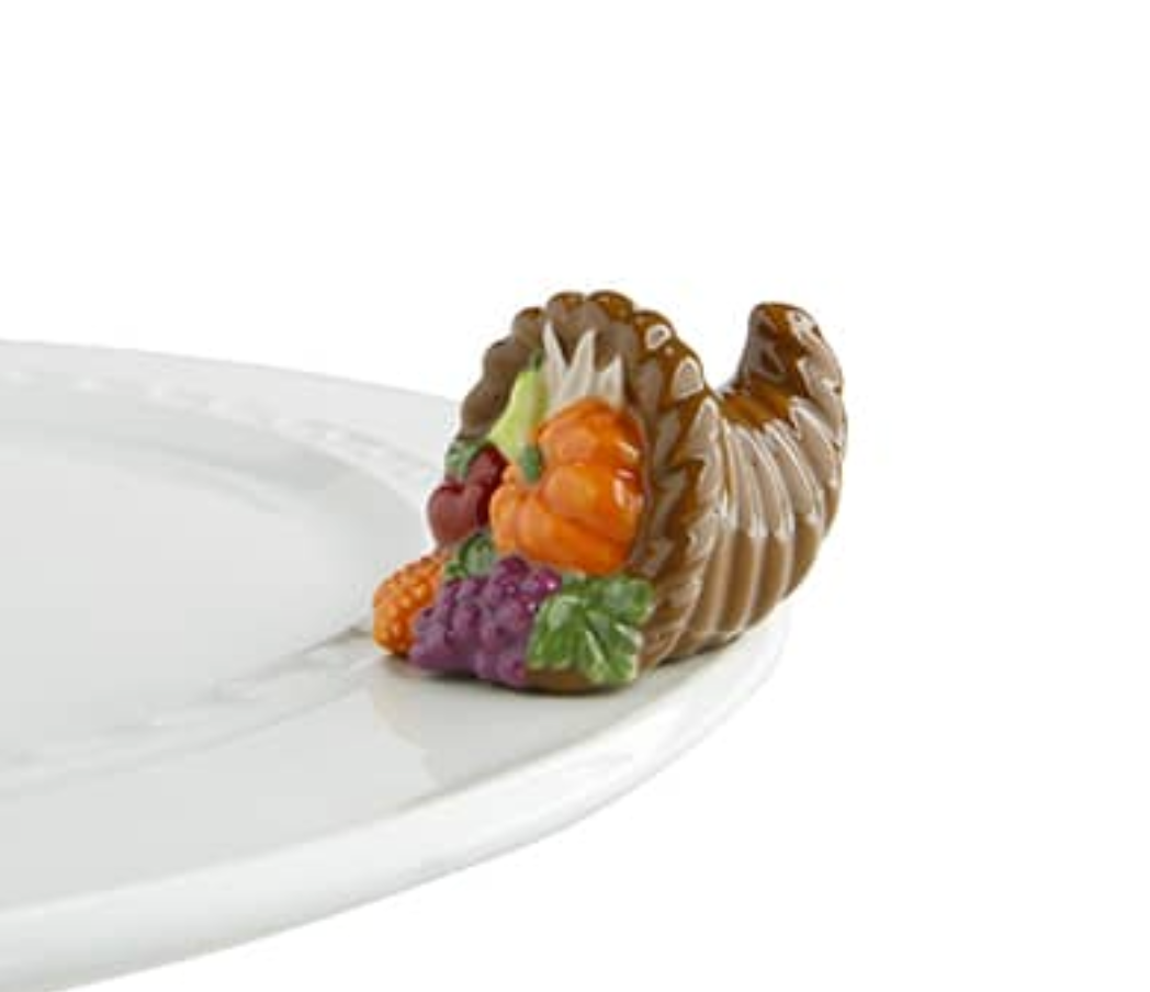 A small, decorative cornucopia-shaped dish charm, featuring autumn-colored fruits such as pumpkin and cranberry, placed on a white plate. Available at Be Charmed