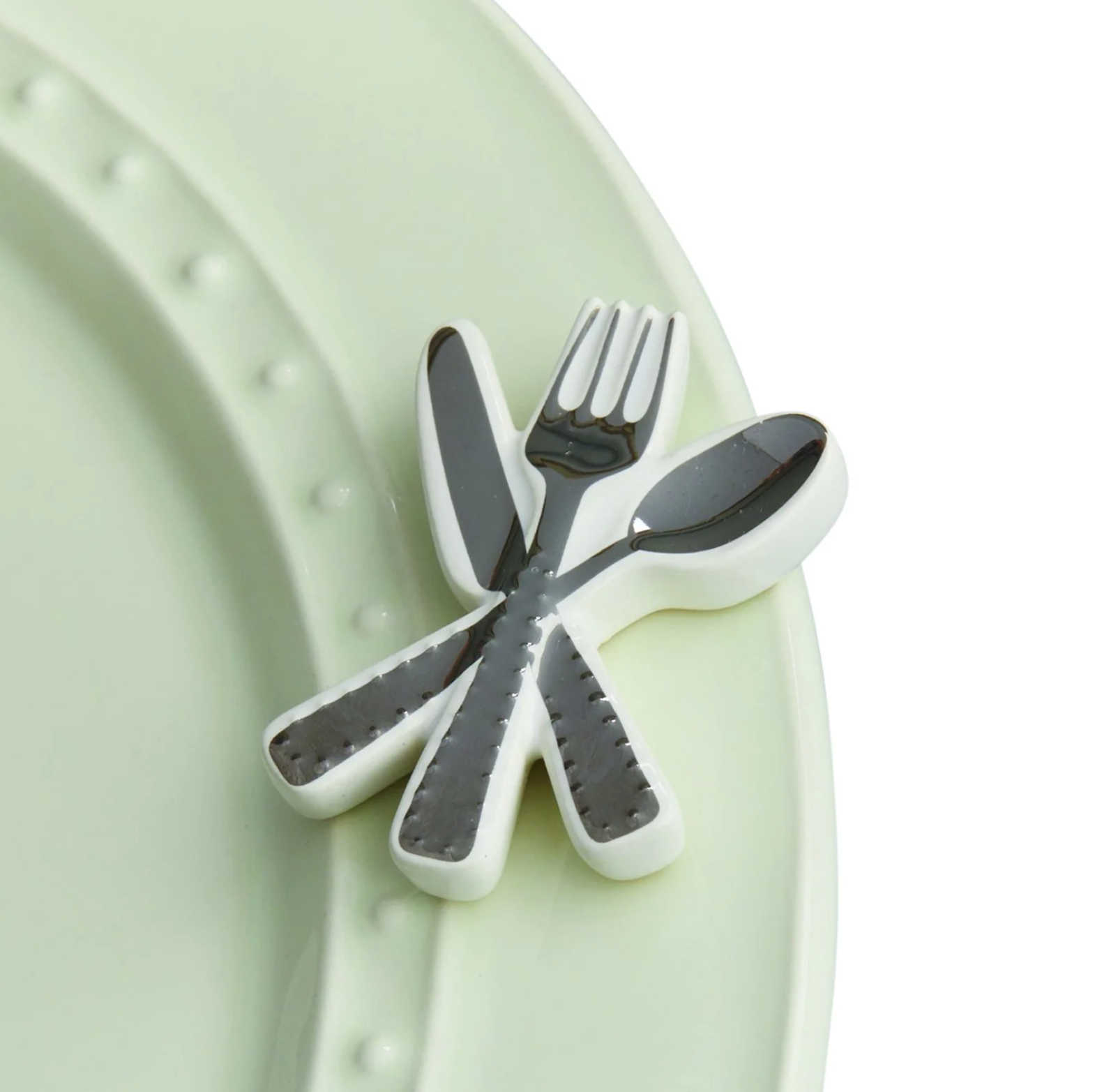 A set of silver-colored miniature cutlery including a fork, knife, and spoon, designed to be used as a charm on a dish. Available at Be Charmed