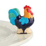 A multicolored rooster-shaped mini charm placed on a white plate. Available at Be Charmed