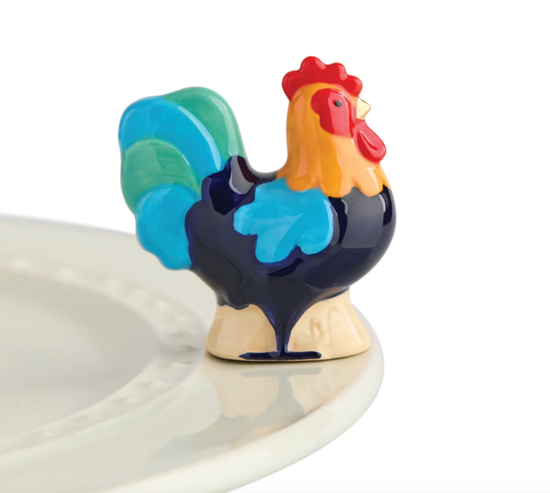A multicolored rooster-shaped mini charm placed on a white plate. Available at Be Charmed
