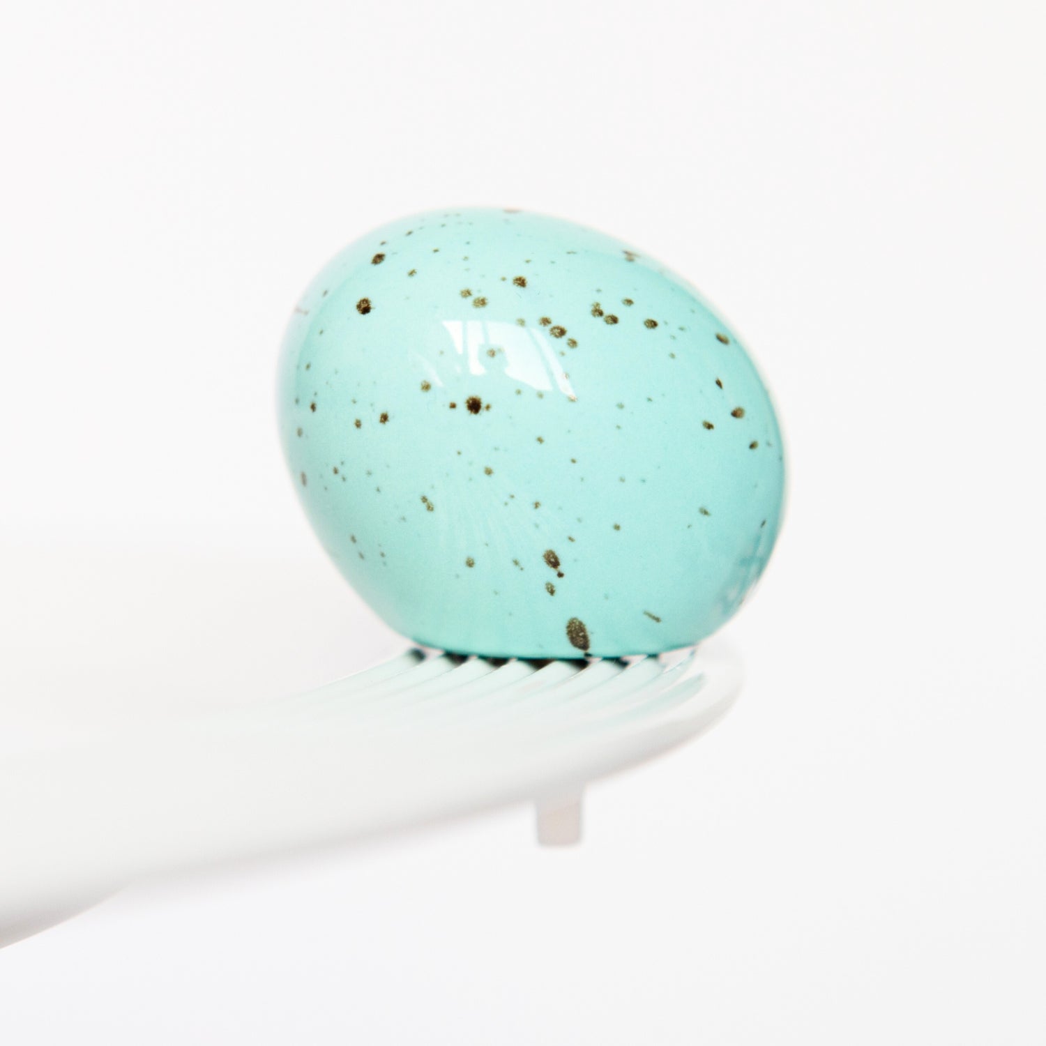 A blue speckled egg-shaped mini charm on a white stand, resembling a Easter egg. Available at Be Charmed