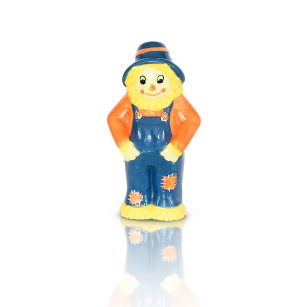A ceramic mini figurine of a smiling scarecrow in blue overalls with orange and white details. Available at Be Charmed