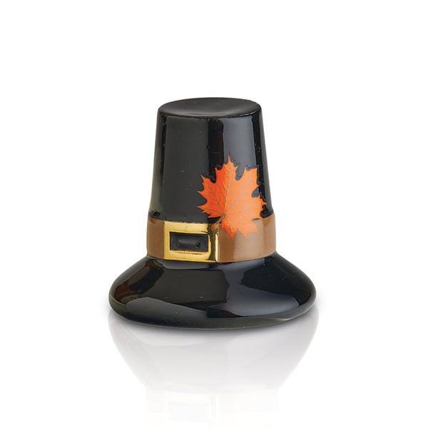 This image features the Nora Fleming Pilgrim Hat Mini, a charming and festive dish accessory. The charm is designed with a deep, glossy black finish and topped with a metallic, gold-colored band . Athat reads "Pilgrim Hat Available at Be Charmed