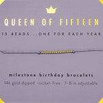 A bracelet with gold-dipped beads on an adjustable cord, labeled 'Queen of Fifteen' and 'Milestone Birthday Bracelets'. Available at Be Charmed