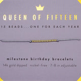 A bracelet with gold-dipped beads on an adjustable cord, labeled 'Queen of Fifteen' and 'Milestone Birthday Bracelets'. Available at Be Charmed
