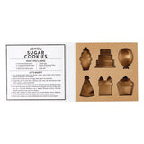Open box of Creative Brands Birthday cookie cutter set in a magnetic book-style box with 6 stainless steel shapes (cake, balloon, candle, present, party hat, heart) and a lemon sugar cookie recipe inside lid—Available at Be Charmed