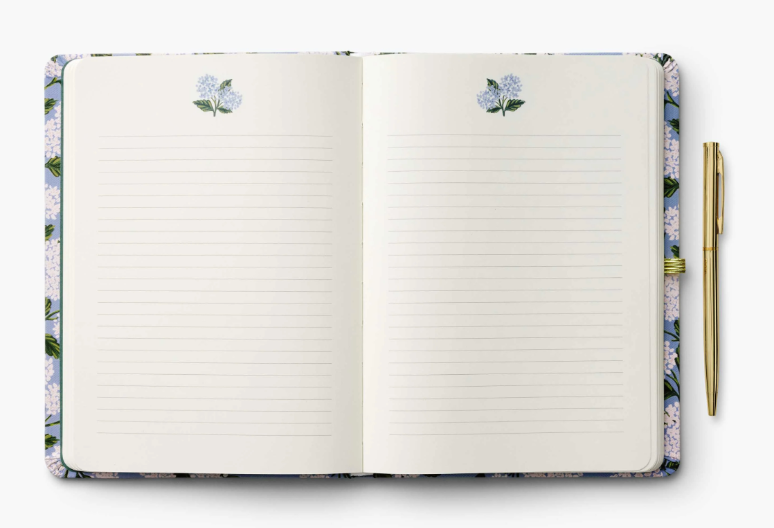 Open notebook with floral design on cover and pen on white background. Available at Be Charmed