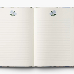 Open notebook with floral design on cover and pen on white background. Available at Be Charmed
