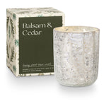 Candle with textured glass and packaging labeled 'Balsam & Cedar' on a white background. Available at Be Charmed