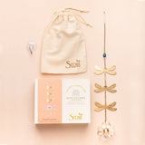 Gold dragonfly suncatcher with packaging and drawstring bag on a beige background. Available at Be Charmed