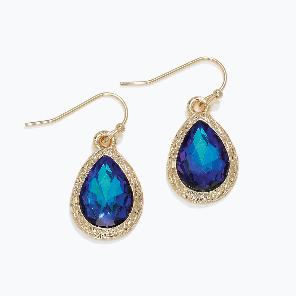 Gold earrings with blue teardrop-shaped gemstones on a white background. Available at Be Charmed