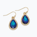 Gold earrings with blue teardrop-shaped gemstones on a white background. Available at Be Charmed