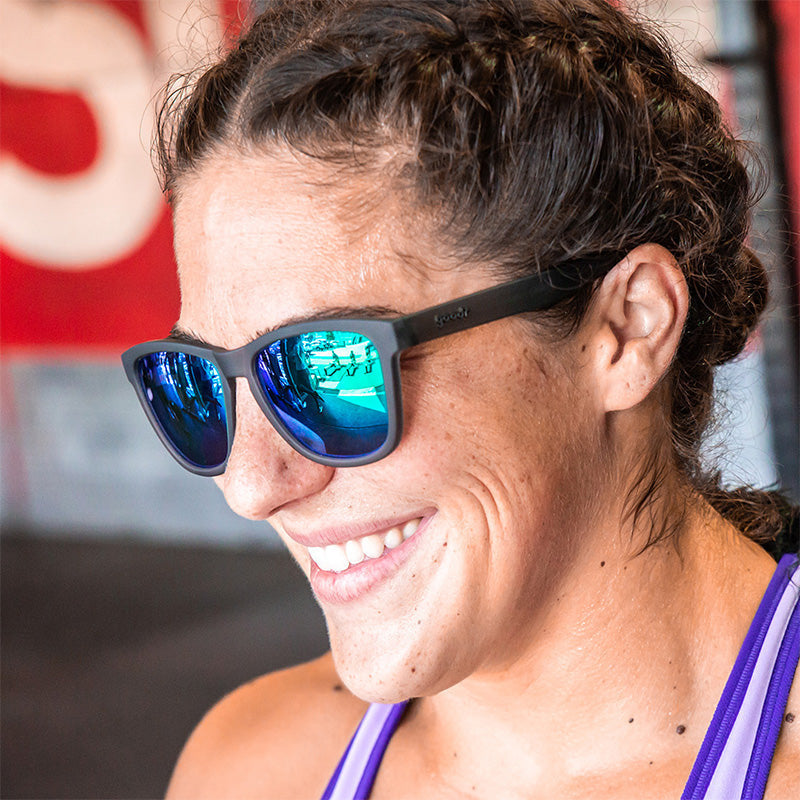 A person wearing Goodr silverback grey and green sunglasses with polarized lenses. Available at Be Charmed