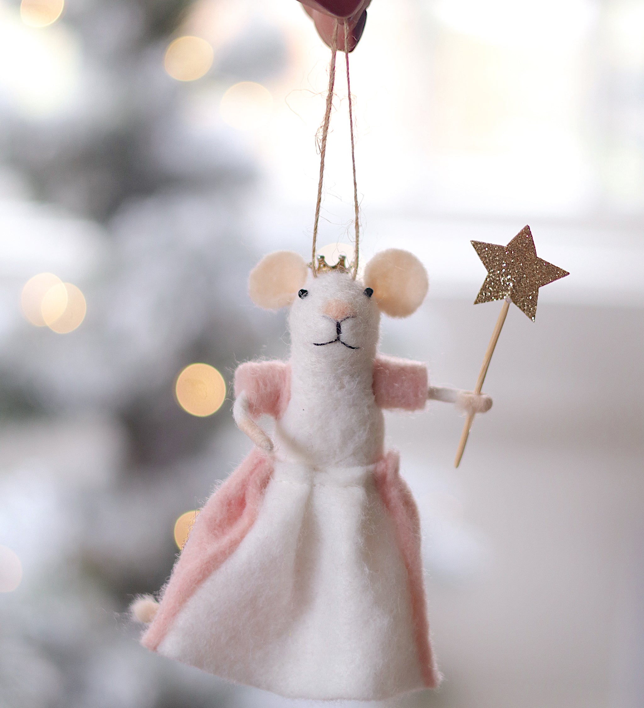 Decorative mouse ornament with a pink skirt and gold star, held against a blurred festive background. Available at Be Chamred