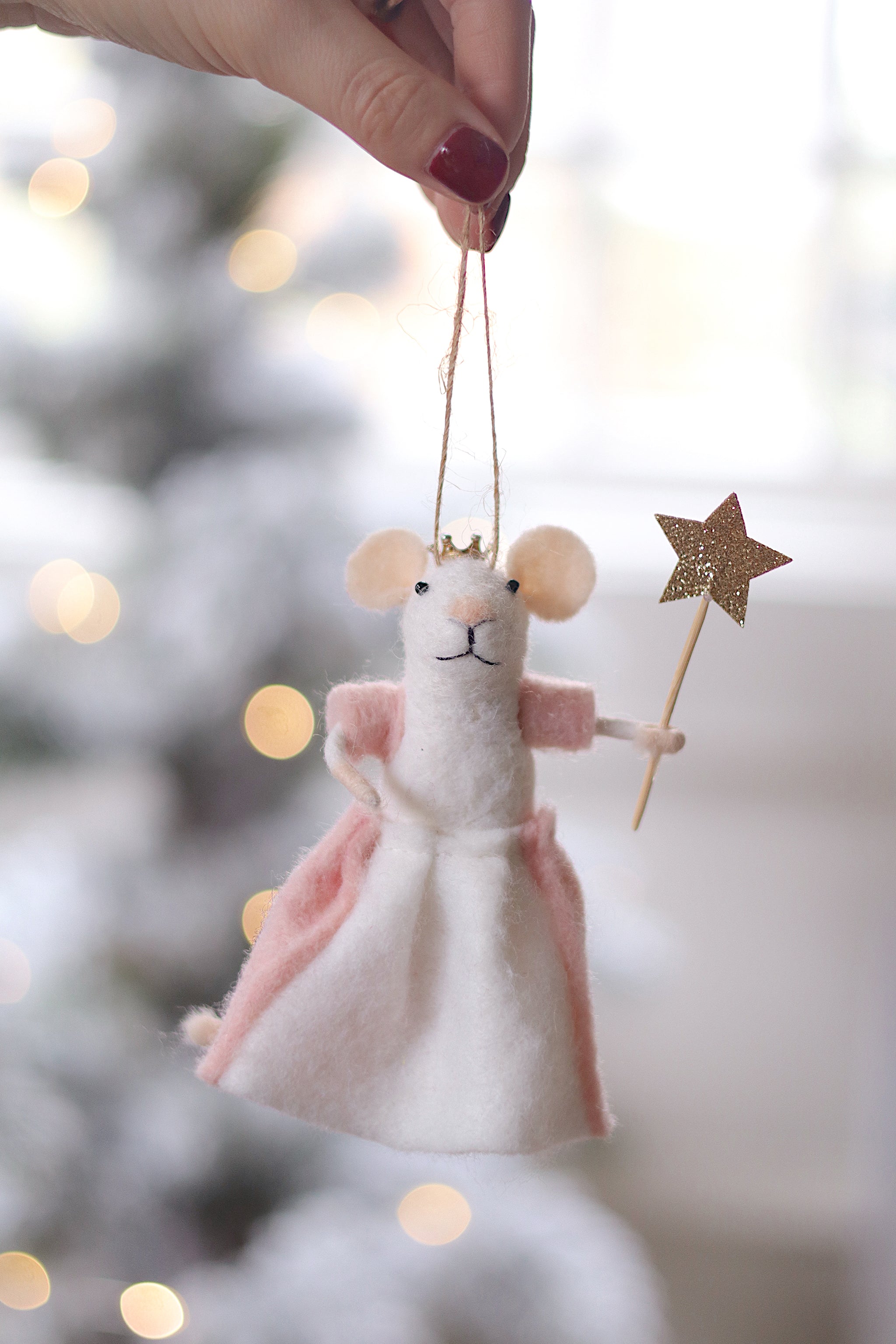 Decorative mouse ornament with a pink skirt and gold star, held against a blurred festive background. Available at Be Chamred