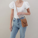 Person wearing a white top and blue jeans with a brown HOBO leather bag on a neutral background. Available at Be Charmed