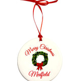 Round white ornament with a green wreath, red bow and ribbon, and red “Merry Christmas” and “Medfield” lettering. Available at Be Charmed.

