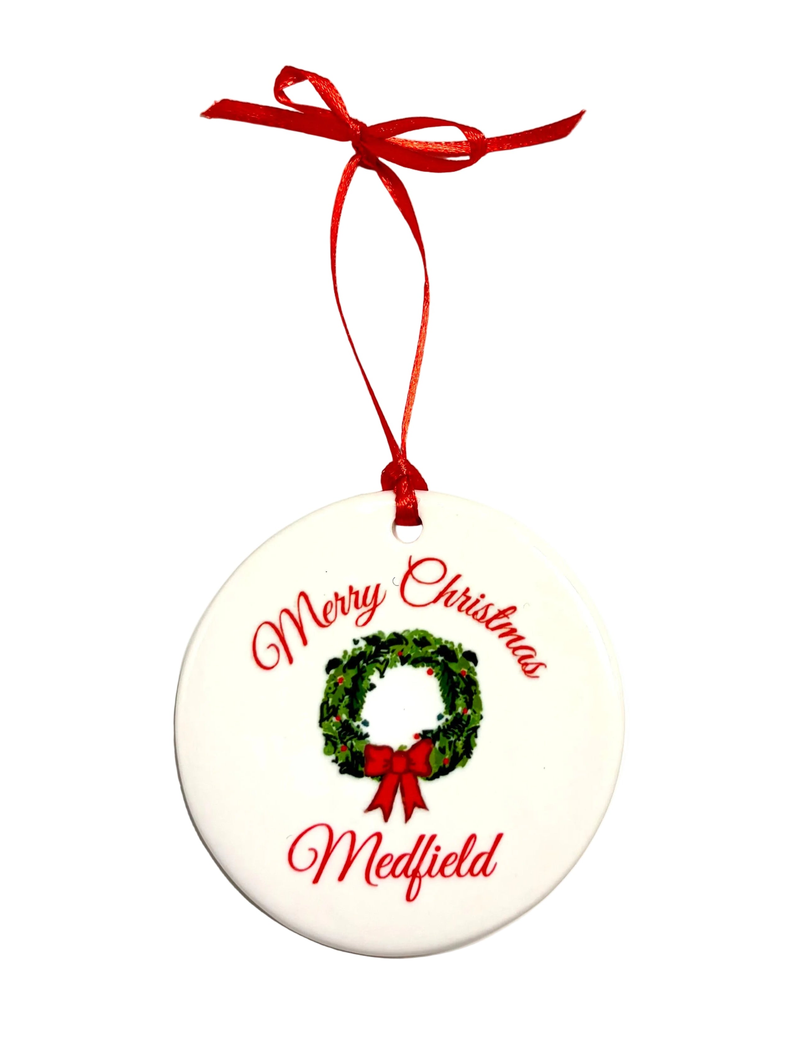 Round white ornament with a green wreath, red bow and ribbon, and red “Merry Christmas” and “Medfield” lettering. Available at Be Charmed.

