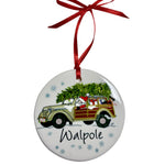  Round white ornament showing Santa driving a woodie wagon with gifts and a Christmas tree, blue snowflakes, “Walpole” lettering and a red ribbon. Available at Be Charmed.

