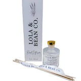 Lola & Bean 4oz Reed Diffuser – Clear glass bottle with gold collar, featuring rattan reeds and a subtle label, available at Be Charmed.