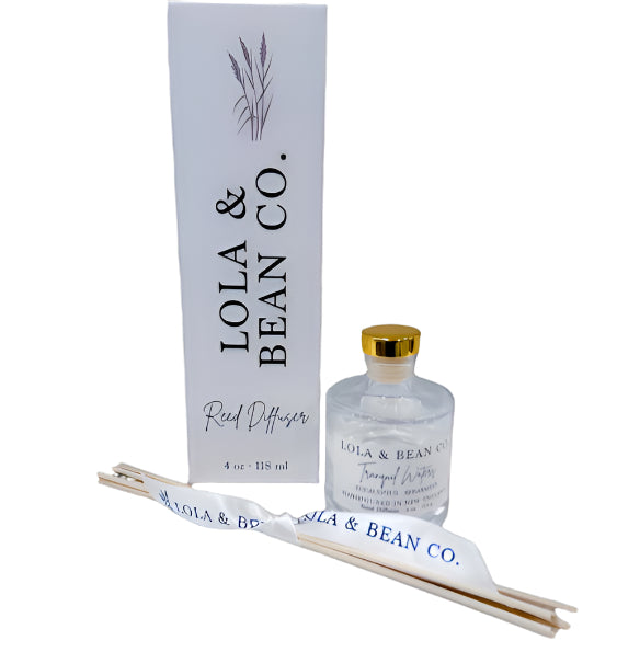 Lola & Bean 4oz Reed Diffuser – Clear glass bottle with gold collar, featuring rattan reeds and a subtle label, available at Be Charmed.