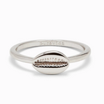 A silver-colored ring with a cowrie shell design on the top, with the phrase 'pura vida' stamped on the inside. Available at Be Charmed