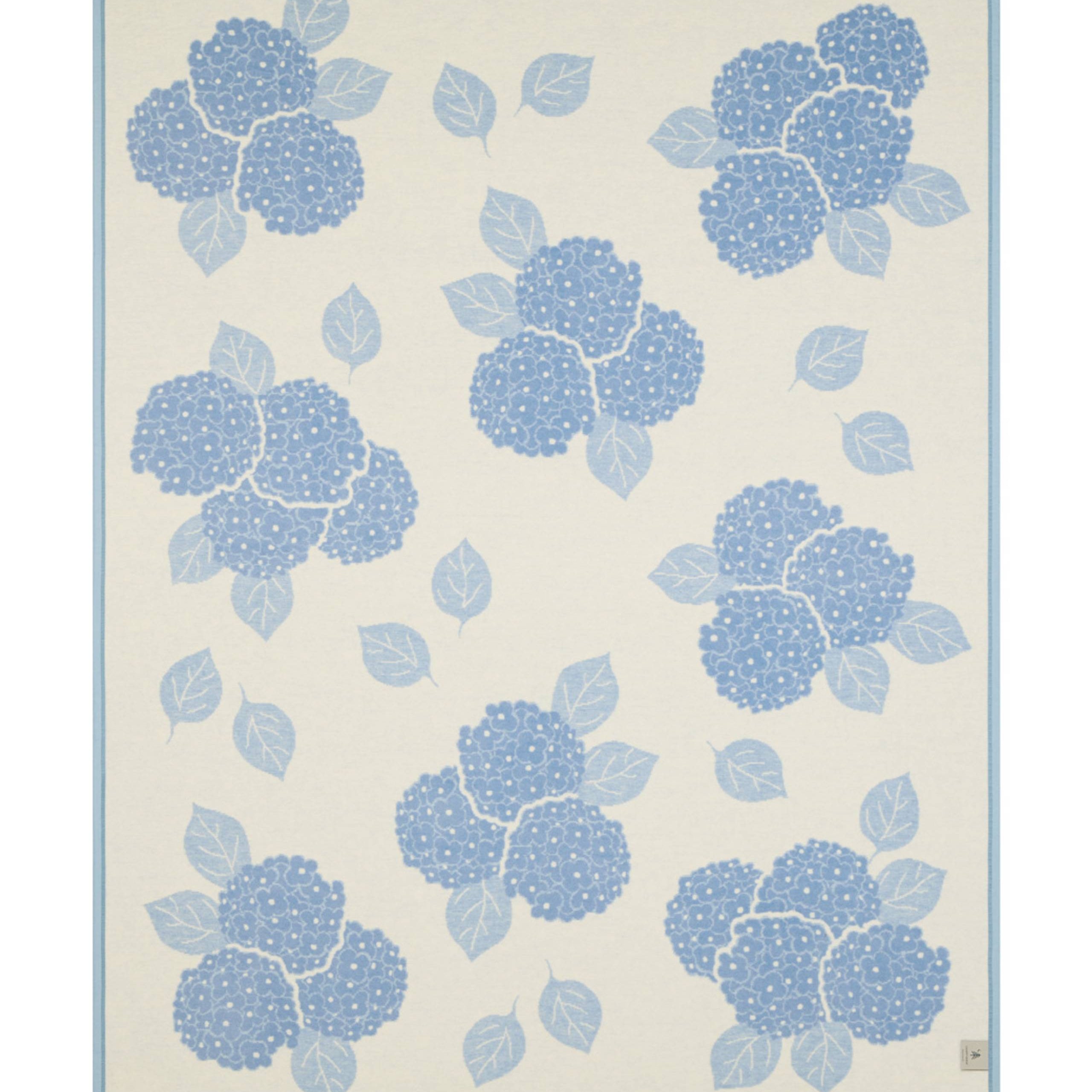 Reverse side of ChappyWrap Hydrangeas Bluebell Blanket featuring soft blue and lavender floral hydrangeas on a cream background. Made from a plush cotton blend for luxurious comfort and durability—ideal for garden-inspired décor or cozy lounging. Available at Be Charmed.