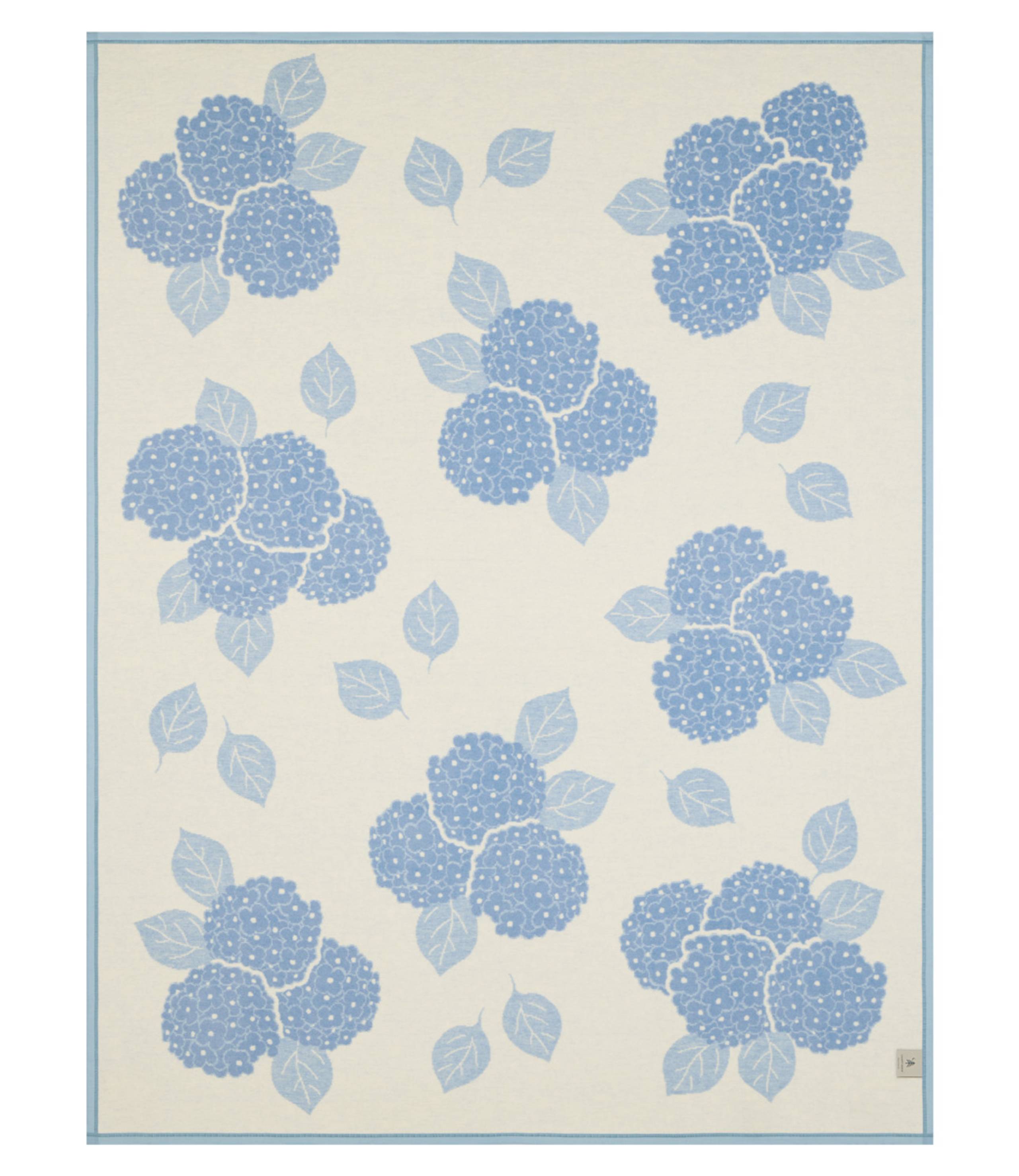Reverse side of ChappyWrap Hydrangeas Bluebell Blanket featuring soft blue and lavender floral hydrangeas on a cream background. Made from a plush cotton blend for luxurious comfort and durability—ideal for garden-inspired décor or cozy lounging. Available at Be Charmed.