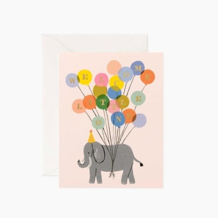 Greeting card with an elephant holding colorful balloons spelling 'Welcome Little One' on a light pink background. Available at Be Charmed