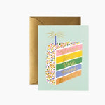 Greeting card with a colorful cake illustration and text, featuring a brown envelope on a white background. Available  at Be Charmed