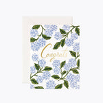 A congratulatory greeting card with a floral pattern and the word 'Congrats' written in a prominent font, accompanied by a white envelope. Available at Be Charmed