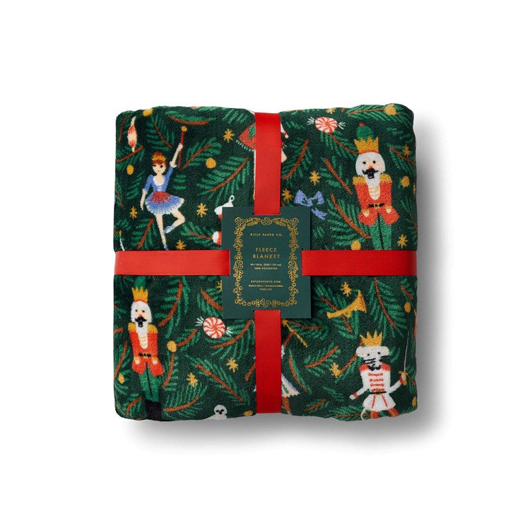 Christmas-themed blanket with Nutcracker design and red ribbon on a white background. Available at Be Charmed