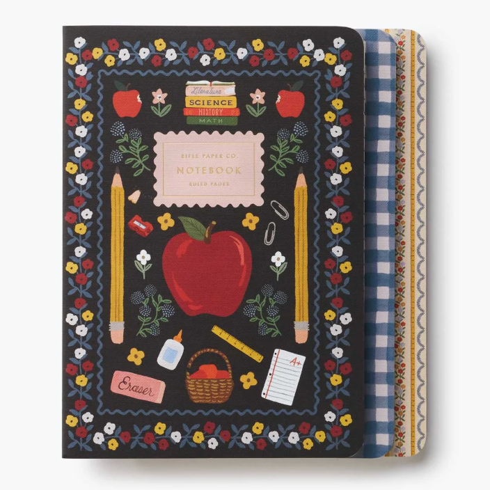 A School themed notebook with a black cover decorated with a colorful floral border, red apple, yellow pencils, and school supplies. The notebook is shown closed with its patterned paper covers partially visible on the right side. Available at Be Charmed